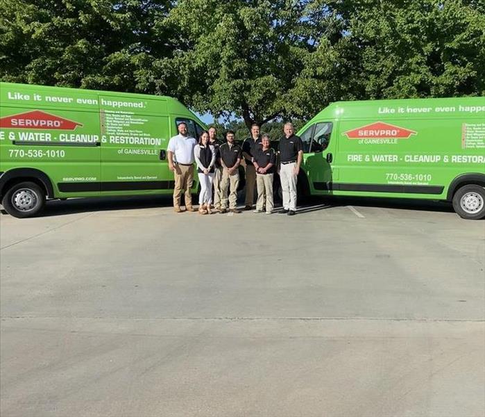 2 green SERVPRO vans nose to nose with group of 7 in front smiling.